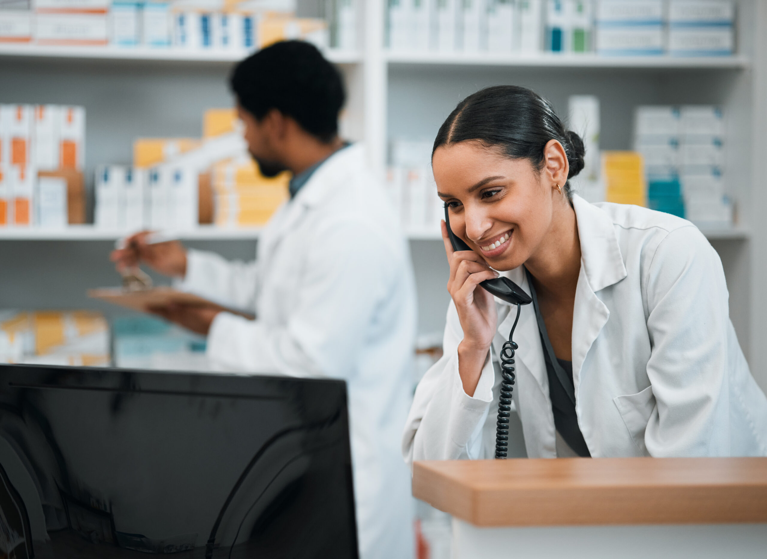 Pharmacist, woman and telephone for medicine stock, customer support and inventory communication or retail service. Medical worker or doctor on phone call and computer for pharmacy or healthcare FAQ.